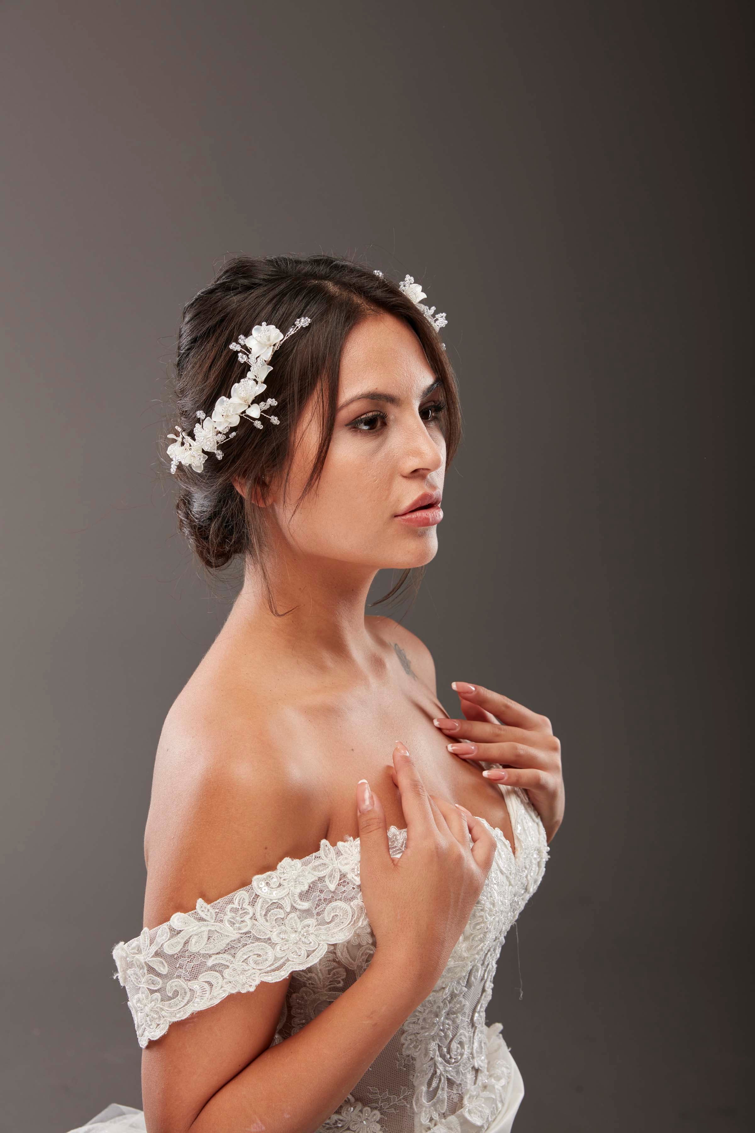 Beyaz romantik çiçek detaylı inci ve kristal gelin saç aksesuarı – topuz saçta yan profil görünüm, omuz açık dantel gelinlik ile uyumlu zarif ve ışıltılı gelin saç tokası