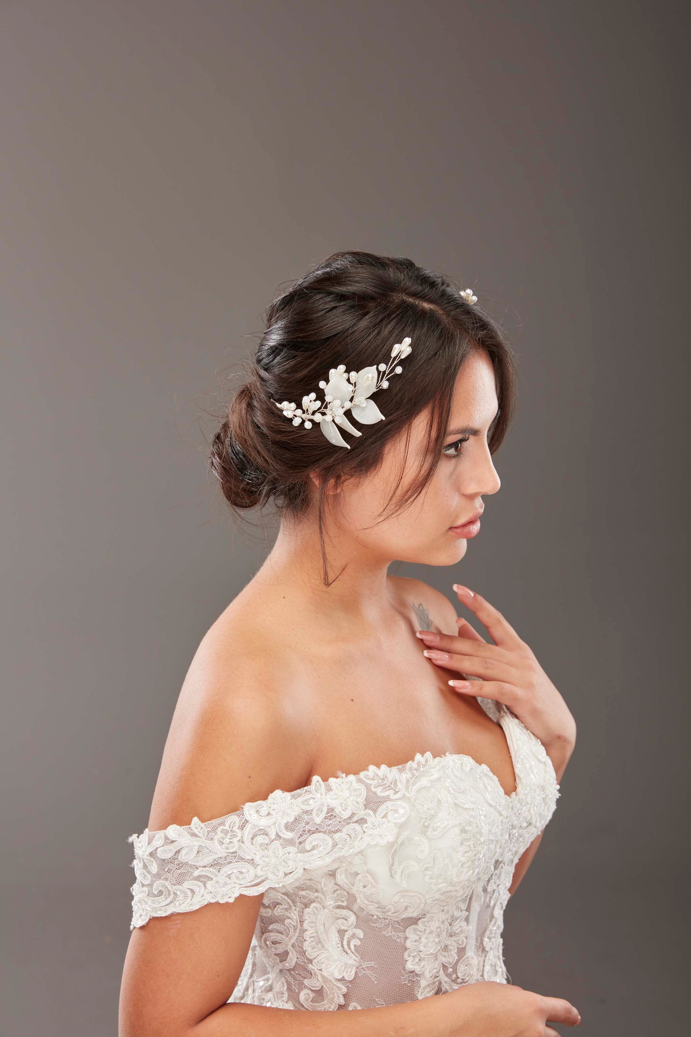 Beyaz minimal çiçek detaylı inci ve kristal gelin saç aksesuarı – topuz saçta yan profil görünüm, beyaz omuz açık dantel gelinlik ile uyumlu zarif ve romantik gelin saç tokası