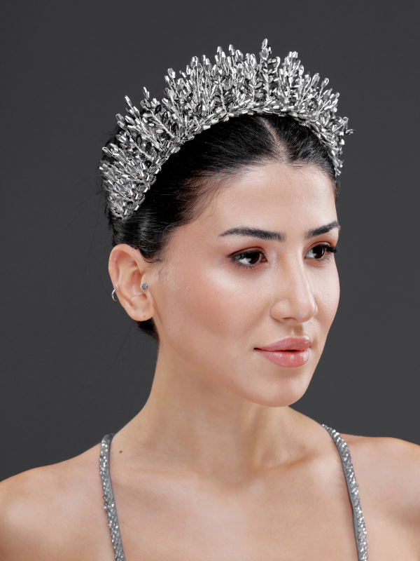 Gri yoğun kristal kraliyet tacı – toplu düz saçta ¾ görünüm, gümüş askılı elbise ile uyumlu modern ve şık gelin saç aksesuarı