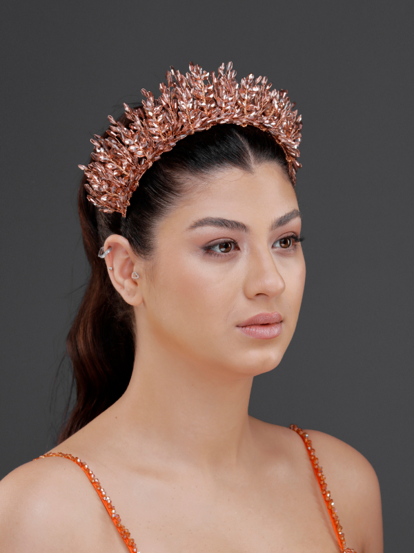 Metalik rose gold yoğun kristal kraliyet tacı – at kuyruğu saçta ¾ görünüm, turuncu askılı elbise ile uyumlu ışıltılı ve modern gelin saç aksesuarı