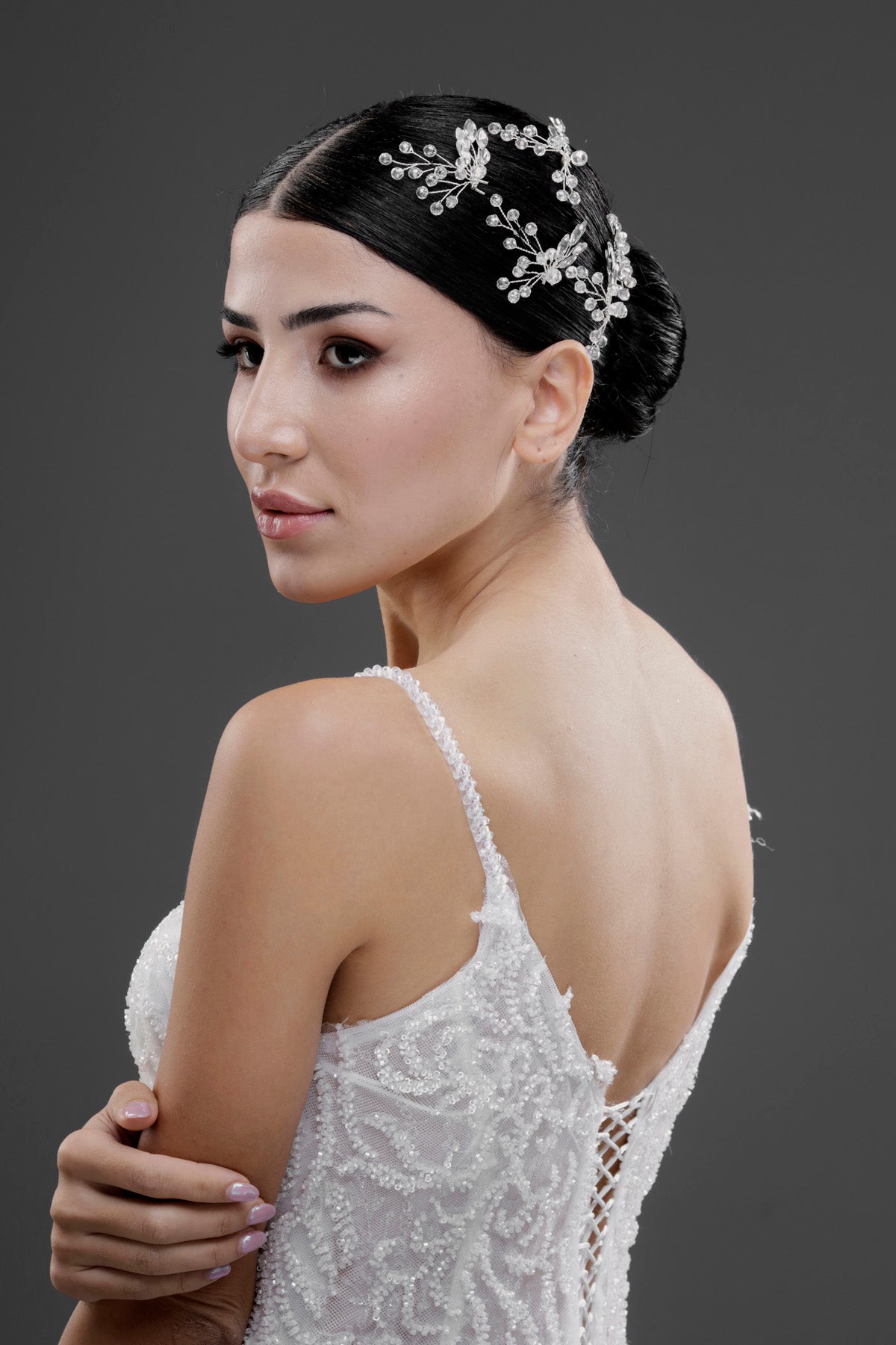 Gümüş kristal dallı gelin saç aksesuarı – düz topuzlu saç modelinde arka-ön görünüm, beyaz dantel sırt dekolteli gelinlik ile uyumlu klasik ve sofistike nikah saç süsü